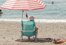 Mand sidder på stranden under parasol