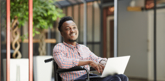 A man sitting in a wheelchair, holding a laptop.
