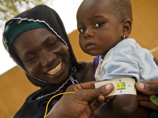 Femme nigérienne tenant dans les bras son enfant. Il porte un bracelet montrant qu'il est sorti de la malnutrition