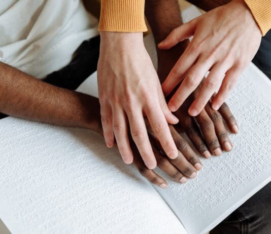 Personnes handicapées - Les mains de deux personnes l’une aidant l’autre à lire le braille