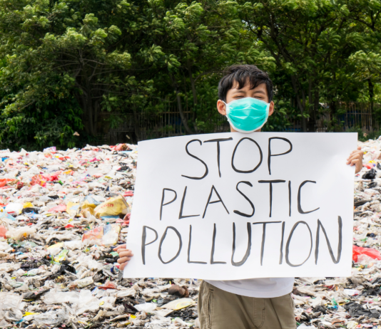 Pollution plastique : vers un nouvel accord international juridiquement contraignant Enfant tenant une pancarte stop à la pollution plastique sur une plage pleine de plastique