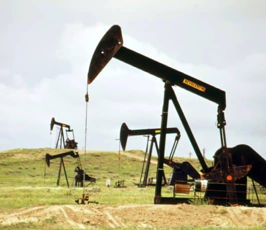 un champ de pétrole. au premier plan, on voit un chevalet de pompage noir. il y en a trois autres à l'arrière plan.