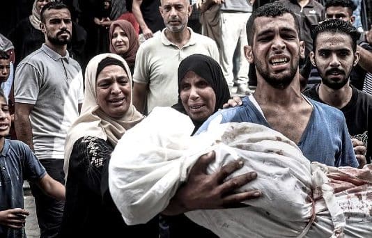 Une famille porte le cadavre enroulé dans un linge blanc d'une jeune femme tuée par une frappe aérienne à Gaza. Des experts estiment qu’Israël commet un génocide à Gaza.