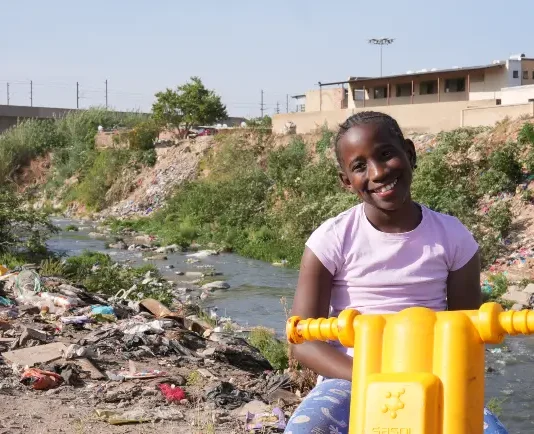 Lotta contro la povertà infantile: i progressi si arrestano a livello globale Il 16 settembre 2025 in Sudafrica, la piccola Ompfuna Nkhumeleni, di 10 anni, posa per un ritratto seduta sulla sua motocicletta di plastica accanto al fiume Juskei, inquinato.