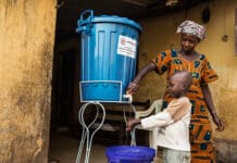 Una madre lava le mani al bambino con acqua trattata con cloro proveniente da un secchio fornito alla famiglia dalla Croce Rossa Internazionale