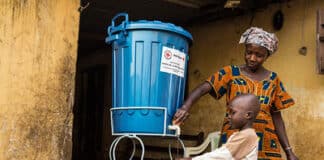 Una madre lava le mani al bambino con acqua trattata con cloro proveniente da un secchio fornito alla famiglia dalla Croce Rossa Internazionale