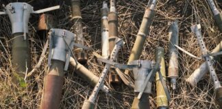 Meerdere gebruikte mortiergranaten en metalen hulzen liggen verspreid op droge grassprieten in een buitenomgeving. Oekraïne