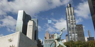 A view of the bronze sculpture "Let Us Beat Our Swords into Ploughshares" by Evgeny Vuchetich, presented to the United Nations in 1959 by the Government of the Soviet Union. In the background is part of the General Assembly building with a sculpture by Ezio Martinelli. UN Photo/Rick Bajornas