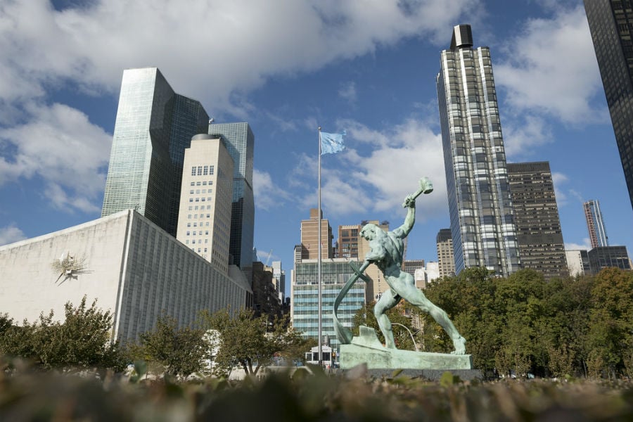 A view of the bronze sculpture "Let Us Beat Our Swords into Ploughshares" by Evgeny Vuchetich, presented to the United Nations in 1959 by the Government of the Soviet Union. In the background is part of the General Assembly building with a sculpture by Ezio Martinelli. UN Photo/Rick Bajornas