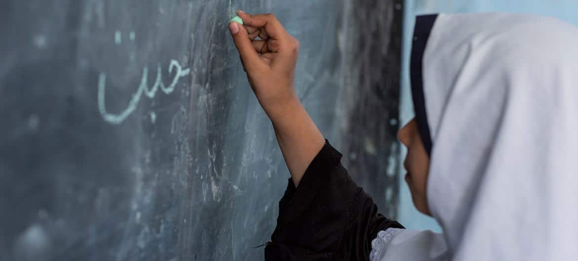 Estudante escrevendo no quadro-negro em uma escola da cidade de Herat, Afeganistão
