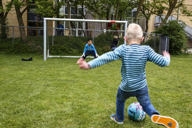 Ett barn som står i ett fotbollsmål och ett som sparkar en boll
